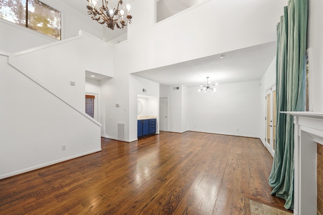 unfurnished living room featuring a towering ceiling, dark wood-type flooring, and a notable chandelier