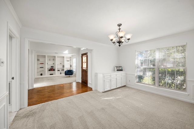 empty room featuring a notable chandelier, built in features, wood-type flooring, and crown molding