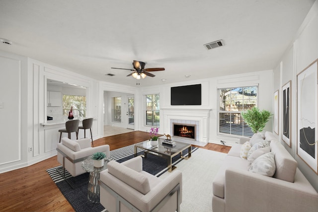 living room featuring a tile fireplace, hardwood / wood-style floors, plenty of natural light, and ceiling fan