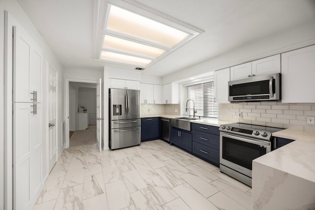 kitchen with tasteful backsplash, light stone counters, stainless steel appliances, sink, and white cabinets