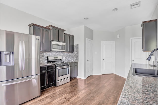 kitchen featuring sink, decorative backsplash, appliances with stainless steel finishes, stone countertops, and wood-type flooring