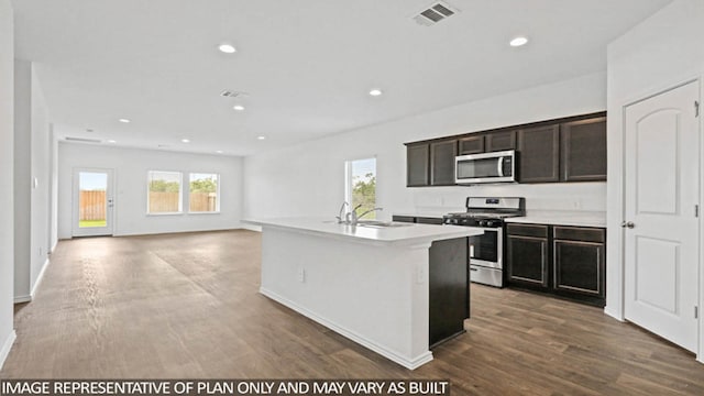 kitchen featuring sink, dark wood-type flooring, stainless steel appliances, an island with sink, and dark brown cabinets