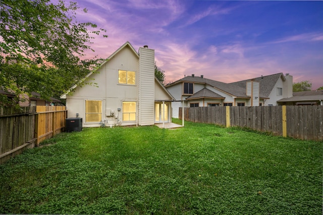 back house at dusk featuring central AC unit and a lawn