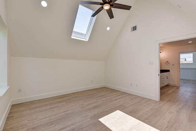 additional living space with vaulted ceiling with skylight, ceiling fan, and light hardwood / wood-style flooring