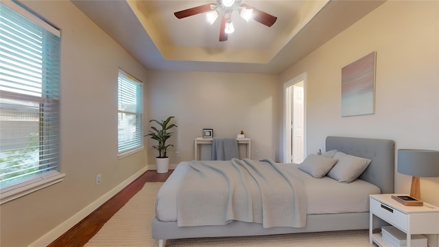 bedroom with hardwood / wood-style floors, ceiling fan, and a raised ceiling