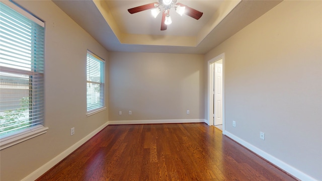 unfurnished room with a tray ceiling, ceiling fan, and dark hardwood / wood-style flooring