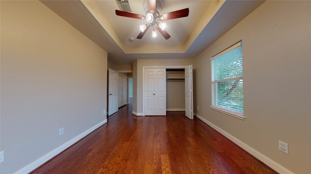 unfurnished bedroom with a tray ceiling, ceiling fan, and dark hardwood / wood-style flooring