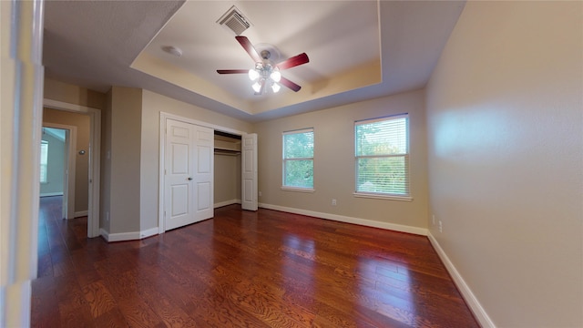 unfurnished bedroom with a closet, dark hardwood / wood-style floors, a raised ceiling, and ceiling fan