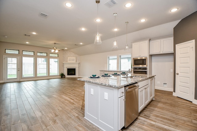 kitchen with lofted ceiling, a center island with sink, hanging light fixtures, appliances with stainless steel finishes, and white cabinetry