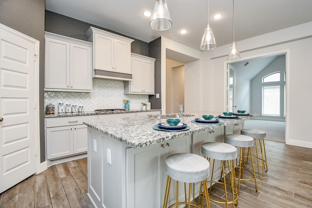 kitchen with sink, pendant lighting, light hardwood / wood-style floors, a kitchen island with sink, and white cabinets