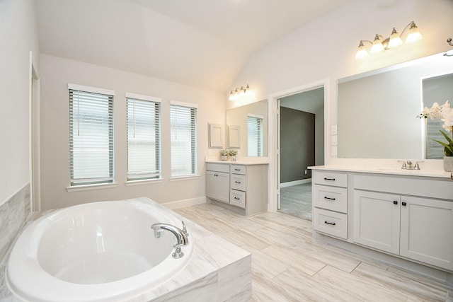 bathroom featuring vanity, lofted ceiling, and tiled tub