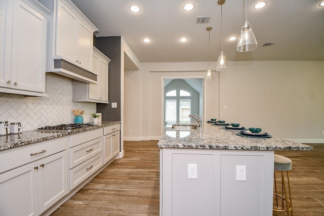 kitchen with decorative light fixtures, light stone countertops, an island with sink, and light hardwood / wood-style flooring