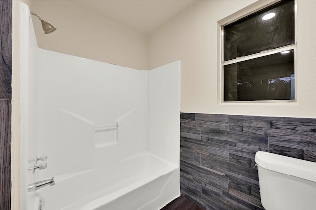 bathroom featuring shower / washtub combination, toilet, and tile walls