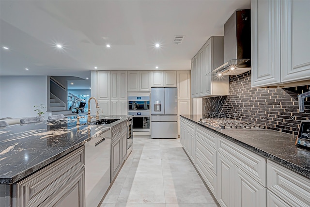 kitchen featuring wall chimney range hood, sink, dark stone countertops, light tile patterned floors, and appliances with stainless steel finishes