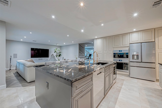 kitchen featuring appliances with stainless steel finishes, a kitchen island with sink, dark stone countertops, and sink