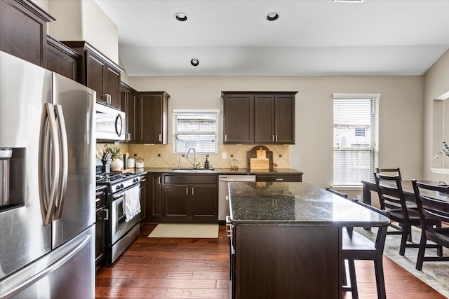 kitchen with a center island, sink, dark hardwood / wood-style floors, dark stone countertops, and appliances with stainless steel finishes