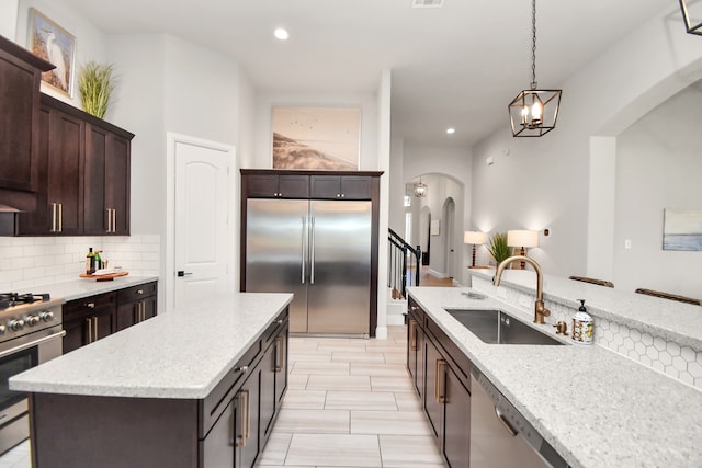 kitchen featuring sink, a center island, stainless steel appliances, light stone counters, and pendant lighting