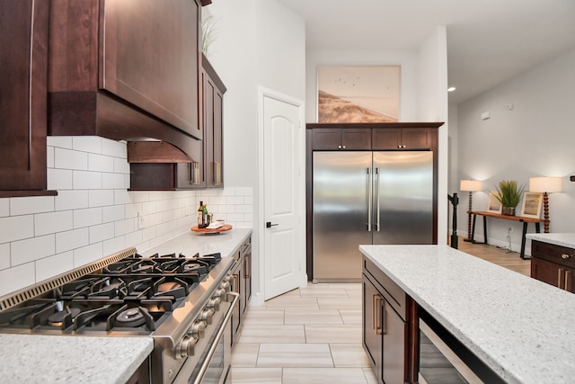 kitchen featuring light stone countertops, dark brown cabinets, tasteful backsplash, and high quality appliances