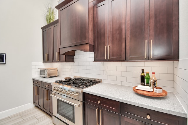 kitchen with custom exhaust hood, high end range, decorative backsplash, light stone countertops, and light hardwood / wood-style floors