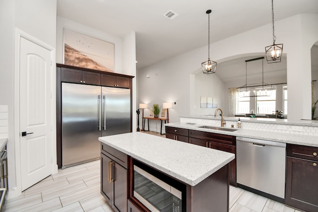 kitchen featuring built in appliances, dark brown cabinetry, sink, and hanging light fixtures