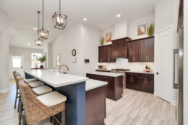 kitchen featuring dark brown cabinetry, high end stove, decorative light fixtures, a breakfast bar, and a center island with sink