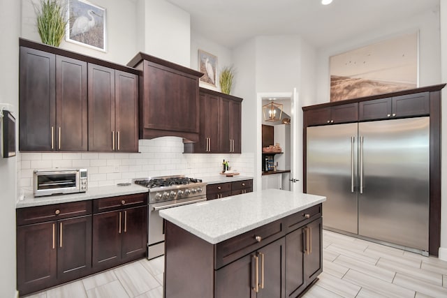 kitchen featuring light stone countertops, tasteful backsplash, dark brown cabinets, high end appliances, and a kitchen island