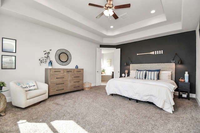 carpeted bedroom with a tray ceiling, ceiling fan, and ensuite bathroom