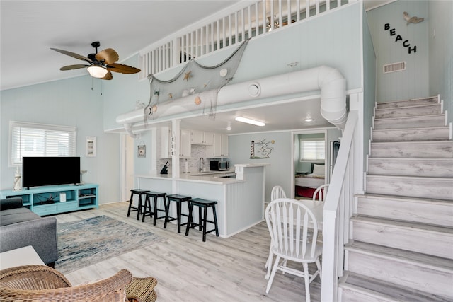 living room featuring ceiling fan, sink, high vaulted ceiling, crown molding, and light wood-type flooring