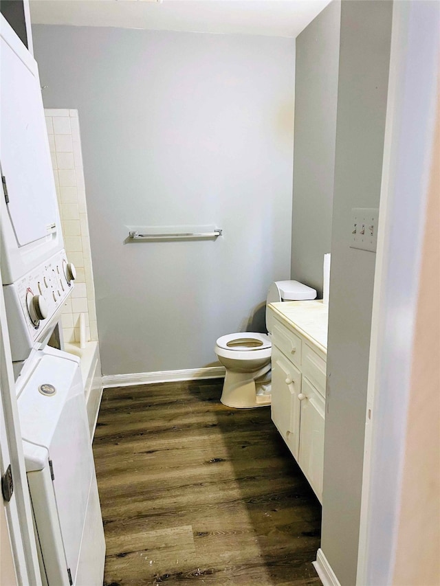 bathroom featuring stacked washer / dryer, vanity, wood-type flooring, and toilet