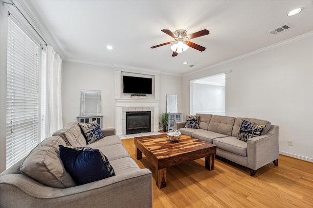 living room with ceiling fan, light wood-type flooring, a fireplace, and ornamental molding