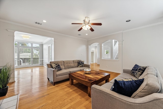 living room with decorative columns, crown molding, ceiling fan, and light wood-type flooring