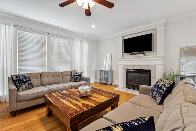 living room featuring crown molding, a fireplace, ceiling fan, and light wood-type flooring