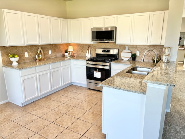 kitchen with kitchen peninsula, appliances with stainless steel finishes, light stone countertops, sink, and white cabinetry