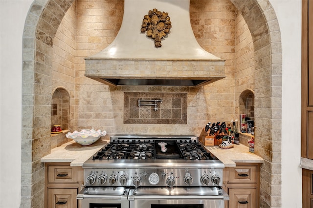 kitchen with high end range, tasteful backsplash, light stone counters, and custom exhaust hood