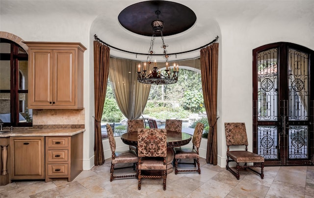 dining room with a raised ceiling, french doors, a wealth of natural light, and an inviting chandelier