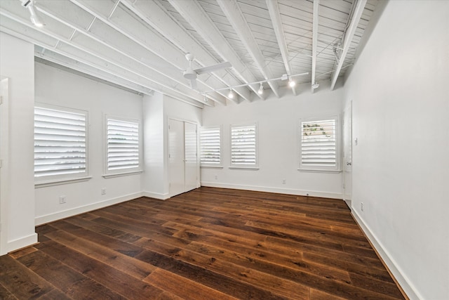 empty room featuring beamed ceiling, a healthy amount of sunlight, and dark hardwood / wood-style flooring