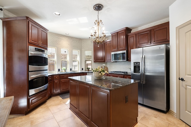 kitchen featuring appliances with stainless steel finishes, decorative light fixtures, a notable chandelier, dark stone countertops, and a center island