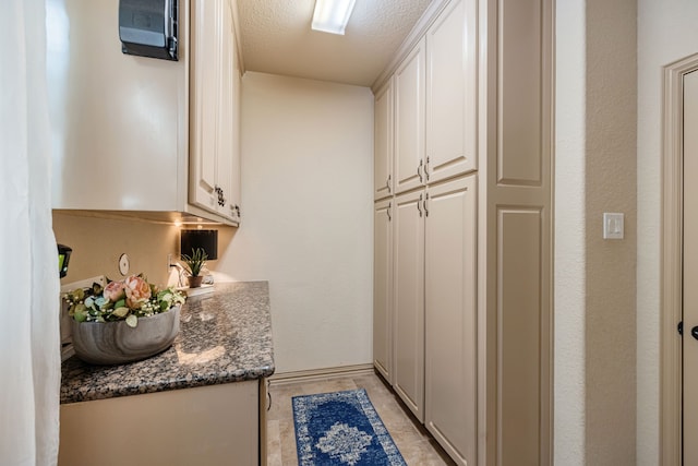 interior space featuring white cabinets, a textured ceiling, and dark stone counters