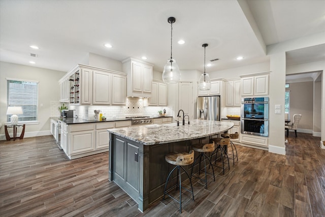 kitchen featuring light stone countertops, dark wood-type flooring, appliances with stainless steel finishes, and an island with sink