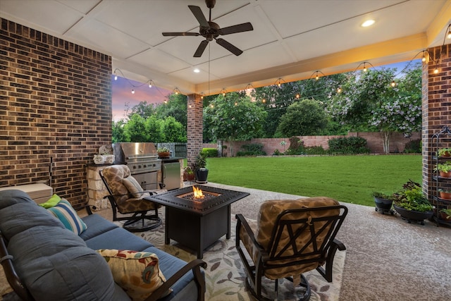 patio terrace at dusk featuring a grill, ceiling fan, a yard, and an outdoor living space with a fire pit