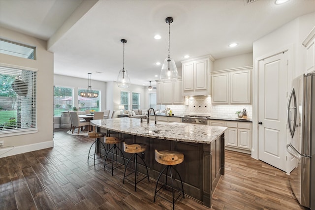 kitchen with white cabinetry, dark wood-type flooring, stainless steel appliances, decorative light fixtures, and a kitchen island with sink