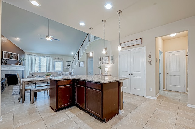 kitchen featuring high vaulted ceiling, ceiling fan, a kitchen island, light stone counters, and a tiled fireplace