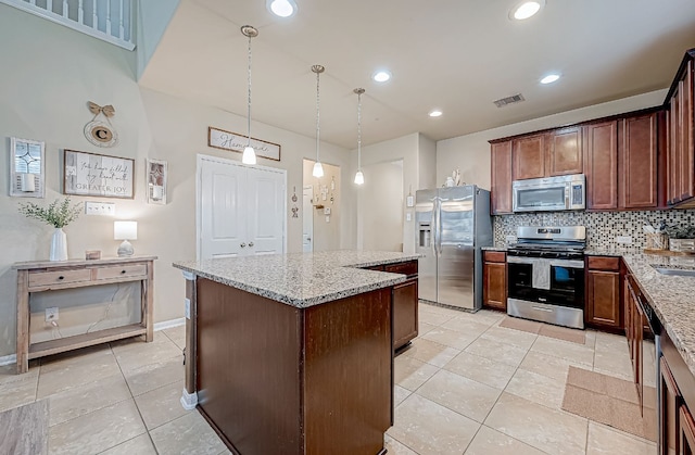 kitchen featuring tasteful backsplash, light stone counters, stainless steel appliances, a kitchen island, and hanging light fixtures