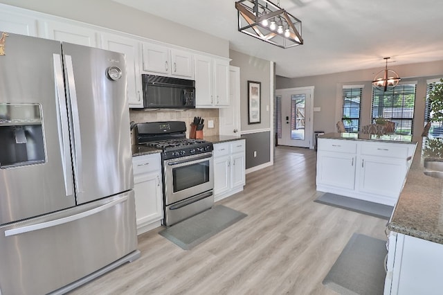 kitchen with appliances with stainless steel finishes, light wood-type flooring, pendant lighting, an inviting chandelier, and white cabinets