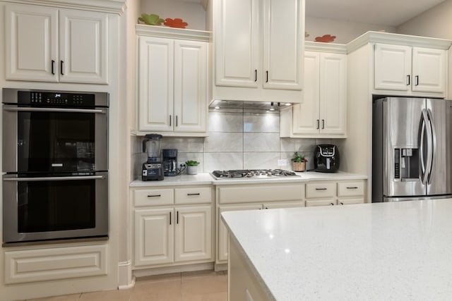 kitchen featuring white cabinets, decorative backsplash, light tile patterned floors, appliances with stainless steel finishes, and light stone counters