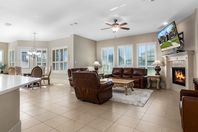 tiled living room with ceiling fan with notable chandelier and a fireplace