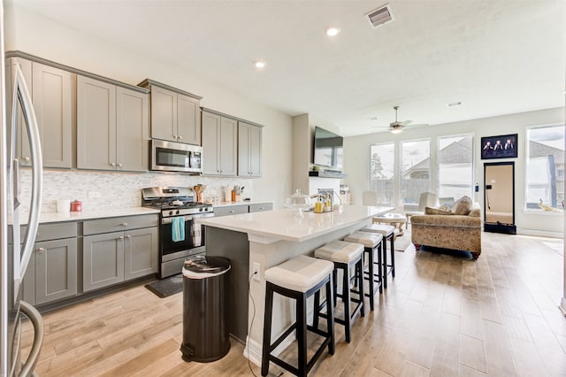 kitchen with gray cabinetry, a kitchen island, light wood-type flooring, and appliances with stainless steel finishes