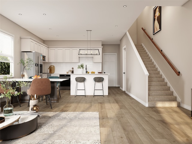 kitchen featuring stainless steel appliances, white cabinets, light hardwood / wood-style floors, a kitchen island, and a breakfast bar area