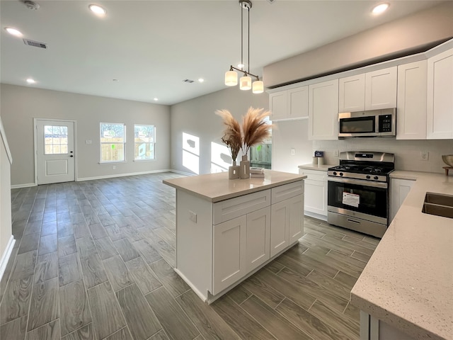 kitchen with white cabinetry, stainless steel appliances, light hardwood / wood-style flooring, pendant lighting, and a kitchen island