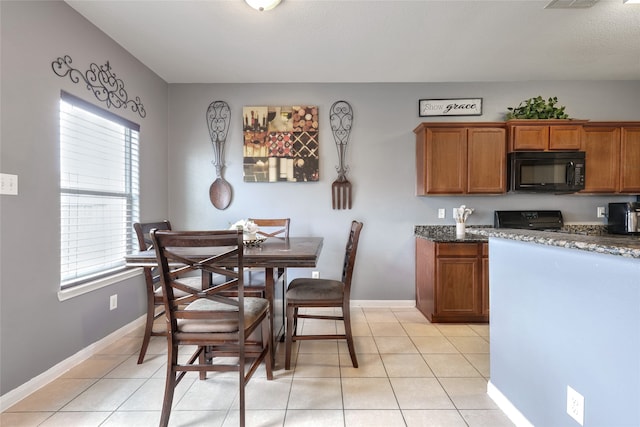 kitchen with light tile patterned floors, dark stone countertops, and black appliances